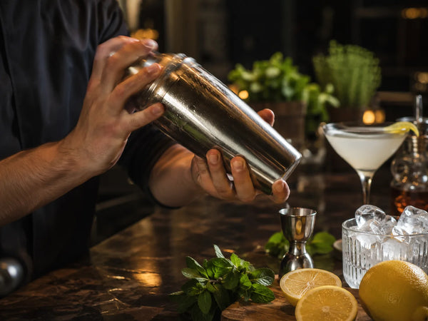 Shaker cocktail en action avec glaçons, citron et accessoires de bar pour préparer un cocktail maison