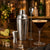 Kit cocktail complet avec shaker et accessoires sur un plan de travail dans une ambiance bar maison chaleureuse